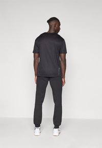 Schwarzes Sport T-Shirt mit kurzen Ärmeln, kombiniert mit schwarzen engen Jogginghosen. Beide aus leichtem Stoff. Weiße Sneakers sichtbar.
