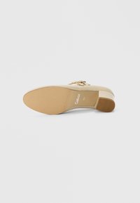Beige højhælet sko med tekstureret sål, der har en gulddetalje og rund tå. Brandlogo trykt på indersålen.