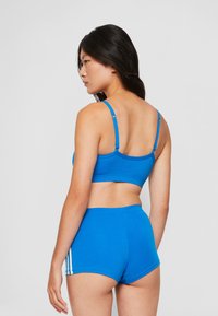 Sujetador deportivo de algodón azul con tirantes ajustables y pantalones cortos azules a juego con franjas laterales blancas. Textura suave, diseño ajustado, estilo minimalista.