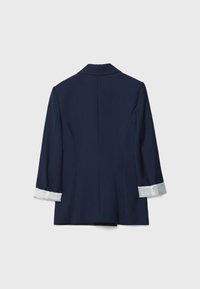 Blazer blu navy con maniche a tre quarti, caratterizzato da un polsino a righe bianche. Design sartoriale con una texture liscia e dettagli minimi.