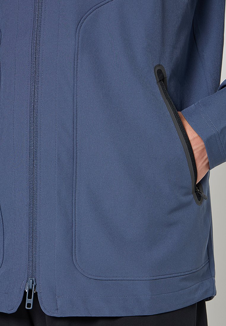 Veste bleu marine en tissu lisse, avec fermeture éclair à l'avant et poches. Présente des accents de fermeture éclair noirs et des détails cousus.