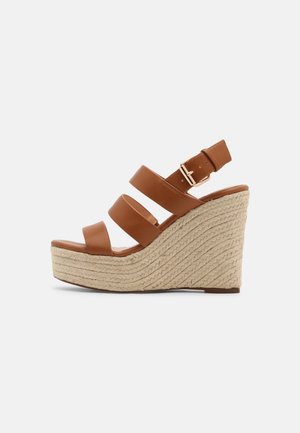 Sandalias cuña de cuero marrón con tres tiras, una hebilla ajustable y una plataforma de yute texturizado, con una forma curva y detalles sutiles.