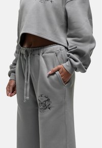 Gestreepte grijze sweatshirt met een ronde hals en een vlinderprint. Grijze trainingsbroek met zijzakken en een trekkoord in de taille. Zachte textuur.