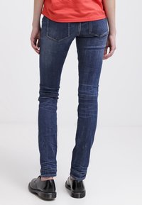 Jeans ajustados en denim azul oscuro, con un diseño de cinco bolsillos, un leve desvanecimiento y una textura suave. Combinados con zapatos negros.