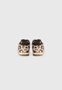 Un paio di sneaker bassi con tessuto a stampa leopardata marrone e crema e suole in gomma, viste da dietro su uno sfondo bianco.
