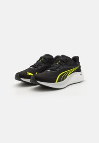 Zapatillas deportivas negras con un empeine de malla texturizada, suela intermedia blanca y acentos en color amarillo neón. Presenta un sistema de cordones tradicional y un collar acolchado.