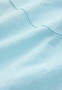 Puha, világoskék szövet sima, enyhén texturált felülettel és finom, varrott varrásvonalakkal, amelyek lágy redőket hoznak létre.