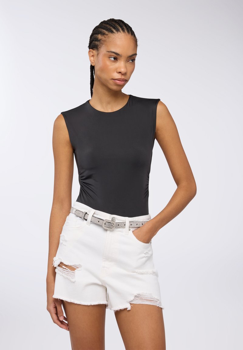 Bodycon senza maniche di colore nero, realizzato in tessuto liscio, abbinato a pantaloni shorts in denim bianco strappati e una cintura argento con una semplice fibbia.
