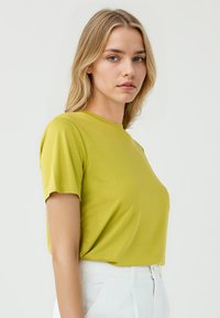 T-shirt a maniche corte, colletto tondo in tessuto verde lime vivace. Morbido al tatto con una vestibilità rilassata, abbinato a pantaloni bianchi a vita alta.
