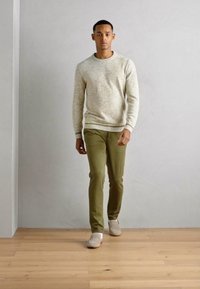 Beige teksturert genser med rund hals, olivengrønne figursydde bukser og lyse sko. Enkelt design med ribbestrikkede mansjetter og nederkant.