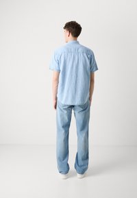 Camisa de denim de manga corta azul claro combinada con jeans azul claro. La camisa tiene un collar y un corte relajado; los jeans tienen un corte recto.