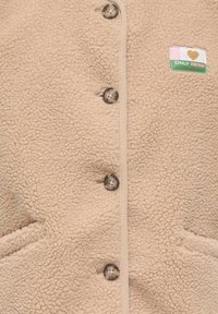 Beeži fliisjope tekstuurse viimistlusega, ees nööpidega ja kahe küljetaskuga. Rinnal nähtav "ONLY VINTAGE" silt.