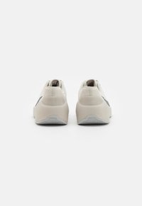 Scarpe da ginnastica leggeri beige con una parte superiore testurizzata, accenti grigi, tacco arrotondato e una suola in gomma con motivo, viste da dietro.
