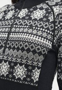 Pull en maille noir et blanc à motifs géométriques et étoiles avec une fermeture éclair à quart au niveau du col.