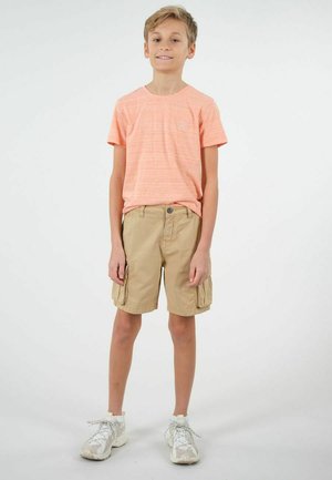 T-shirt léger à manches courtes et rayé orange clair, associé à un short en toile beige avec plusieurs poches, complété par des chaussures de sport blanches.