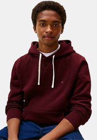 Felpa borgogna in misto cotone, con cappuccio e cordino di regolazione, polsini a costine e un piccolo logo sul petto. Design slim fit.