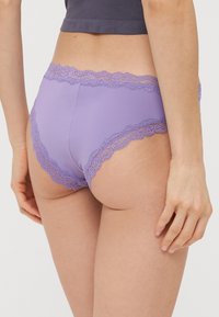 Fialové dámské kalhotky s hladkým materiálem a ozdobnou krajkou podél pasu a otvorů pro nohy. Mají středně vysoký střih.