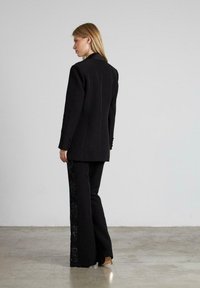 Blazer negro con un corte entallado y mangas largas, combinado con pantalones negros que tienen una franja lateral de lentejuelas. Textura suave, sin patrones discernibles.