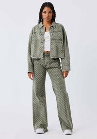 Groene geblokte denimjacket gecombineerd met bijpassende high-waisted broek. De jacket heeft een cropped ontwerp en een rafelige zoom; de broek is wijd.