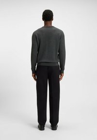 Maglione in grigio carbone a maglia con collo rotondo, polsini e orlo a coste, abbinato a pantaloni neri a gamba dritta e scarpe nere. Vista da dietro.