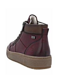 Botín de tobillo de cuero rojo con un acabado texturizado, cierre de cremallera lateral y un cuello acolchado. Cuenta con una suela de goma de color marrón claro.