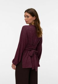 Bordo dolga majica z dolgimi rokavi in pasom za zavezovanje v pasu. Mehka, teksturirana tkanina z udobnim krojem. Posebnost na hrbtni strani in padajoči rokavi.