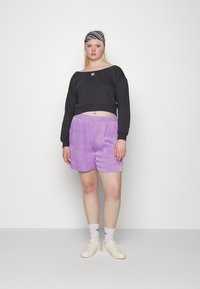 Sweatshirt cropped preto com logotipo branco, combinado com calções lilás claros. Ténis brancos e uma faixa de cabelo estampada completam o look.