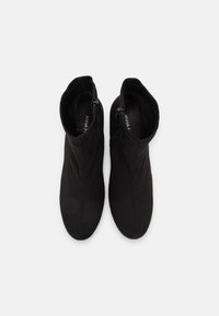 Černé kotníkové boty vyrobené z měkké semišové kůže, s hladkým povrchem, zakřivenými vršky a bočními zipy pro snadné obouvání. Žádné viditelné detaily hardwaru.