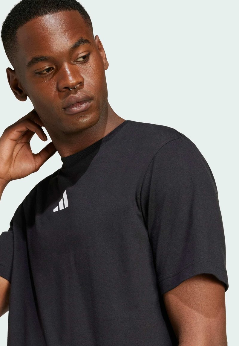 Svart kortärmad t-shirt i bomull med rund halsringning och vitt Adidas-logga på bröstet. Slät textur, avslappnad passform.