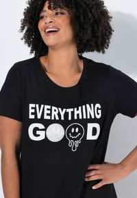 Czarny bawełniany t-shirt z wyraźnym białym napisem "EVERYTHING GOOD" oraz grafikami uśmiechniętych buziek. Okrągły dekolt, krótkie rękawy, swobodny krój.