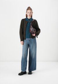 Brown knit cardigan, teal button-up shirt, wide-leg blue jeans, black ankle boots, and a burgundy crossbody bag. Minimalist design.