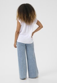 Weiße Leinenbluse mit rohen Kanten, kombiniert mit hellblauen, weit geschnittenen Jeans aus Denim, die eine lockere Passform und eine glatte Textur aufweisen.