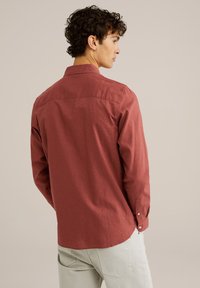 Cămașă roșie cu mâneci lungi, cu guler tip buton, fabricată dintr-un material din bumbac, având un tiv drept și manșete cu buton. Textură netedă, fără modele.
