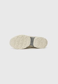 Sneaker sole with a textured, patterned design. Material is rubber in off-white and gray. Features a prominent brand logo in the center.