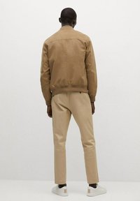 Brun bomberjakke, beige slim bukser og hvide sneakers. Glat tekstur med minimal hardware; afslappet design, rene linjer og neutrale farver.