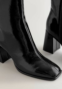 Black patent leather ankle boots with a square toe and block heel, featuring a side zipper and a glossy finish.