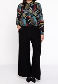 Pantalones negros de pierna ancha combinados con una camisa de manga larga con estampado floral multicolor que presenta un cierre con botones en la parte delantera y cuello.