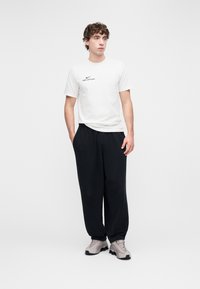 Balti medvilninė marškinėliai su juodu užrašu „NIKE OFFICIAL“, derinami su laisvomis juodomis sportinėmis kelnėmis ir šviesiai pilkais sportbačiais.