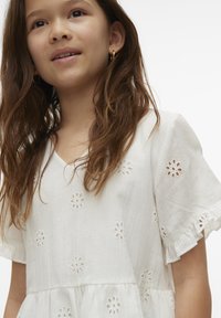 Abito di cotone bianco con ricami floreali, maniche corte a balze e scollatura a V. La texture morbida e il design a strati ne esaltano l'aspetto.