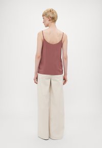 Top sin mangas de color rosa con tirantes finos, combinado con pantalones anchos beige; textura de tela suave con un mínimo de detalles.