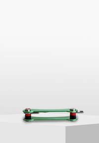 Green metal tool with a flat shape, featuring red and black accents, and circular hardware at either end. Smooth surface finish.