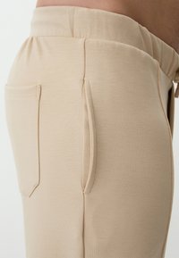 Beige joggers made of soft, stretchy fabric, featuring a wide elastic waistband and two inset side pockets for casual wear.
