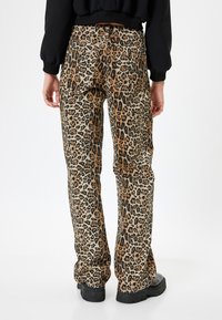 Leopard print pants in tan and black with a relaxed fit. Features back pockets and a straight leg design. Material appears denim-like.