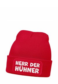 Red knitted beanie hat with ribbed texture. Features a white patch displaying the text "HERR DER HÜHNER" in bold letters.