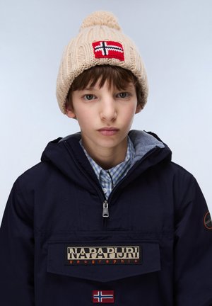 Junge mit beigefarbener Strickmütze mit norwegischem Flaggenaufnäher und marineblauer Napapijri-Jacke mit Logos und Reißverschlusskragen.