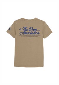 T-shirt di cotone beige con maniche corte. Grande stampa blu sulla parte posteriore con la scritta "The Dnm Association" e ulteriore testo sottostante. Presenta un piccolo logo sulla manica.