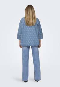 Svijetloplavi traper jakna s uzorkom srca, 3/4 rukavima i opuštenim krojem, uparen s ravnim svijetloplavim farmerkama.