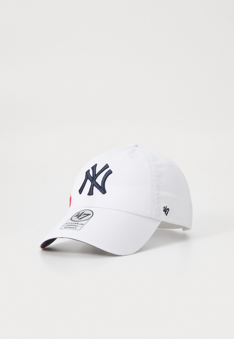 Gorra de algodón blanca con el logotipo "NY" bordado en azul marino, visera curva y acento rojo. Presenta una etiqueta de marca en el frente y el lado.