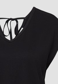 Zwarte mouwloze top met V-hals en dunne straps die achteraan in een strik zijn gebonden, weergegeven tegen een effen lichte achtergrond.