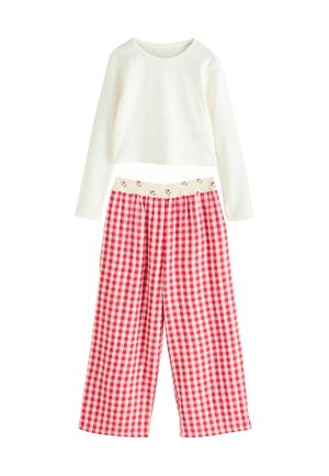 Biała bluzka z długim rękawem o prążkowanej fakturze, w połączeniu z czerwono-białymi spodniami dresowymi w kratkę vichy z elastycznym pasem w kwiaty.